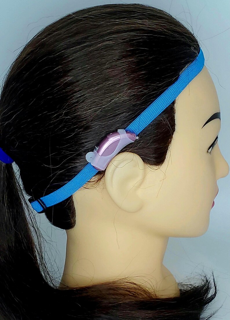 May include: A blue headband with a small pink hearing aid attached to the side.
