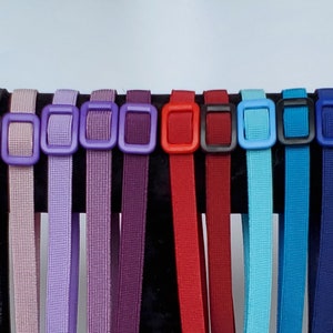 May include: A display of colorful, adjustable straps with square plastic buckles. The straps are in various colors, including beige, brown, black, purple, red, teal, pink, and blue. The straps are hanging from a black display stand.