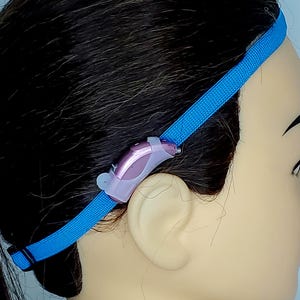 May include: A blue headband with a hearing aid attached to it. The headband is made of a soft, stretchy material and has a secure fit. The hearing aid is small and discreet, and it is designed to be comfortable to wear for extended periods of time.