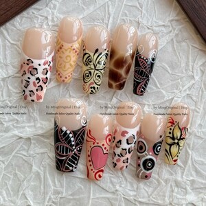 Puede incluir: Un conjunto de diez uñas artificiales con varios diseños. Las uñas presentan patrones como estampado de leopardo, floral y arte abstracto en colores como rosa, negro, amarillo y marrón. Las uñas se muestran sobre una superficie blanca texturizada.