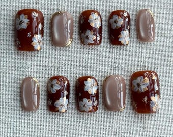 May include: Set of ten false nails with a brown and white floral design. Some nails have a light brown shimmer finish.