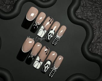May include: A set of ten long, coffin-shaped press-on nails with a Halloween theme. Designs include a black spider, a white pumpkin, a ghost face, and a spiderweb. The nails have a nude base with black and white accents. The text "Ming Original" is visible.