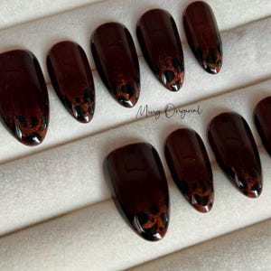 May include: Set of ten brown almond-shaped press-on nails with a black and brown leopard print design.