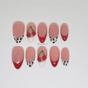 May include: Set of ten false nails with a red and white french manicure design. Some nails feature a black and white leopard print design, while others have a 3D cherry design.