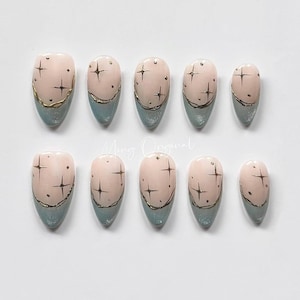 May include: Ten light pink almond-shaped press-on nails with a gold glitter design. The nails have a light blue base.