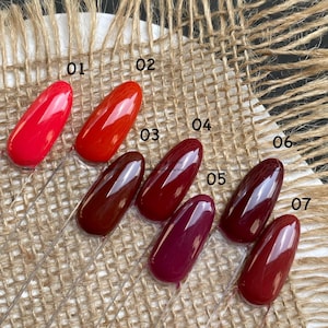 May include: Seven oval-shaped nail polish swatches displayed on clear plastic sticks, numbered 01 through 07. The colors range from bright red at 01 to deep burgundy and dark wine shades at 07, all featuring a glossy, smooth finish on each tip.