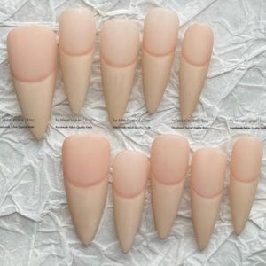 Può includere: Un set di dieci unghie press-on in una tonalità nude color pelle con una forma a stiletto appuntita. Ogni unghia presenta una finitura opaca liscia e una linea cuticolare curva. Il testo "by MingOriginal | Etsy Handmade Salon Quality Nails" è visibile.