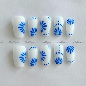 May include: A set of white press-on nails with a matte finish. Each nail is decorated with a blue floral design. The nails are in various shapes and sizes, with the text "Ming Original" printed at the bottom.