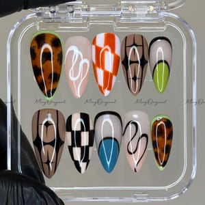 May include: A set of ten artificial nails in a clear plastic case. The nails feature various designs, including a brown and black leopard print, white swirls, orange and white checkered patterns, and geometric shapes. The text "Ming Original" is visible.