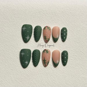 May include: Set of ten green and nude false nails with various Christmas-themed designs, including snowflakes, holly leaves, and a knitted pattern. The nails are arranged in two rows on a white surface.