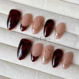 Puede incluir: Conjunto de diez uñas postizas con un diseño de caparazón de tortuga y oro. Las uñas son de forma ovalada y tienen un acabado brillante.