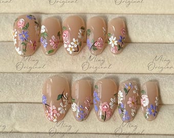 May include: Set of ten nude-coloured false nails with a floral design. The nails feature a variety of pink, purple, and white flowers with green stems and leaves.