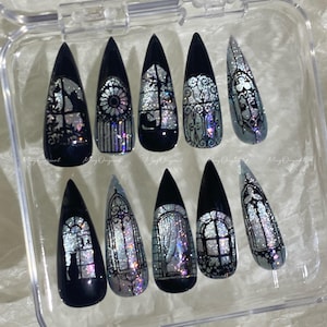 May include: Set of ten black and silver press-on nails with a gothic window design. Each nail features a different window design with silver glitter accents. The nails are almond-shaped and displayed in a clear plastic case.