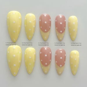 May include: A set of ten press-on nails in various sizes. The nails feature a mix of designs, including yellow with white polka dots and pink with white polka dots. The nails are almond-shaped and have a glossy finish.