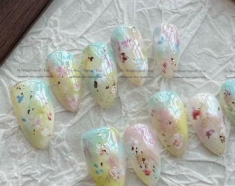 May include: A collection of ten artificial nails featuring a floral design. Each nail has a gradient of yellow, pink, and blue, decorated with tiny flowers and gold leaf. The text "by MingOriginal | Etsy Handmade Salon Quality Nails" is visible.