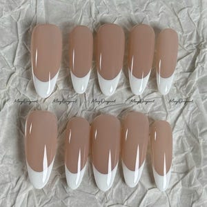Pode incluir: Um conjunto de dez unhas postiças com um design clássico de manicure francesa. Cada unha apresenta uma base de cor nude e uma ponta branca. O texto "Ming Original" está impresso na superfície do papel.