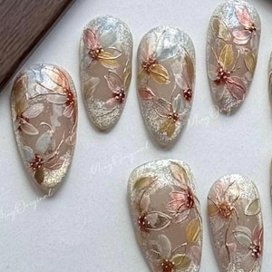 Peut inclure: Ensemble de faux ongles avec un motif floral. Chaque ongle présente une base transparente avec des paillettes argentées et des fleurs multicolores délicates dans les tons de rose, jaune et vert. Les ongles sont de forme ovale.