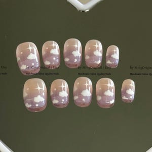 May include: Set of ten press-on nails with a sky-themed design. Each nail features a gradient of peach and purple, with white cloud and star accents. The nails are oval-shaped and have a glossy finish.