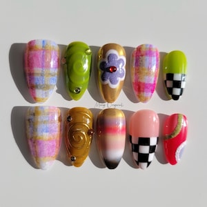 Op de afbeelding: Set van tien kunstnagels met verschillende ontwerpen. De ontwerpen omvatten ruitjes, geruit, swirl, bloem en abstracte patronen. De nagels zijn in tinten roze, groen, goud en rood.