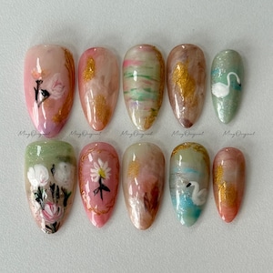 May include: A set of ten almond-shaped artificial nails with various designs. The nails feature floral patterns, gold accents, and a swan design. The color palette includes pink, green, gold, and white. The text "Ming Original" is printed on each nail.