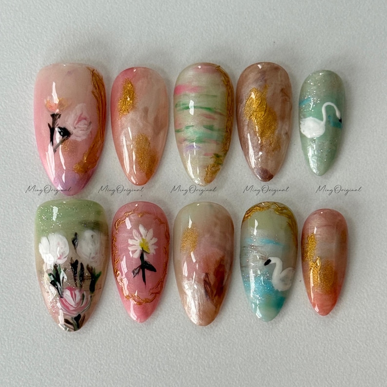 May include: A set of ten almond-shaped artificial nails with various designs. The nails feature floral patterns, gold accents, and a swan design. The color palette includes pink, green, gold, and white. The text "Ming Original" is printed on each nail.