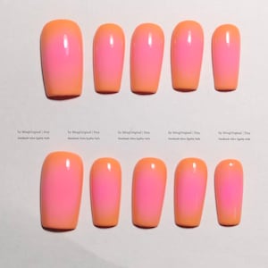 Puede incluir: Un conjunto de uñas postizas con un diseño degradado. Las uñas hacen la transición de un naranja brillante en la base a un rosa vibrante en la punta. Las uñas están dispuestas en dos filas de seis, mostrando la transición de color.