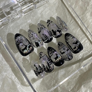May include: A set of ten artificial nails with a winter holiday theme. Each nail features a black base with silver glitter and a design of trees, deer, and snowflakes. The nails are oval-shaped and displayed in a clear plastic case.