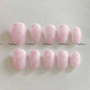 May include: Set of ten oval-shaped, light pink press-on nails with a marbled effect. Each nail has a glossy finish. The text "Ming Original" is printed on the image.