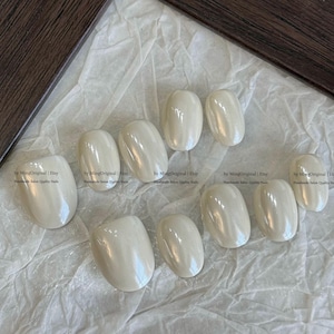 May include: A set of ten press-on nails with a smooth, pearlescent off-white finish. Each nail features a rounded oval shape and a glossy, reflective surface. The text "by MingOriginal | Etsy Handmade Salon Quality Nails" is visible on the image.