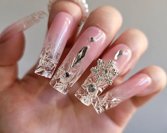 Puede incluir: Uñas acrílicas largas de color rosa y transparente con adornos de copo de nieve y cristal.