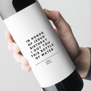 May include: A white wine bottle label with the text "In honour of Jesus' birthday I got you this bottle of water".