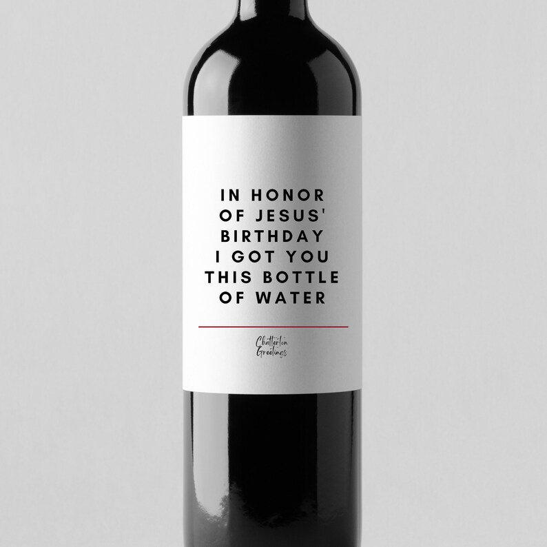 May include: A white wine bottle label with black text that reads "In honour of Jesus' birthday I got you this bottle of water". The label also includes the text "Chatterbox Greetings" in a smaller font.