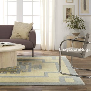 Pode incluir: Um tapete azul claro e amarelo com um design geom&eacute;trico. O tapete est&aacute; em uma sala de estar com um sof&aacute; e uma cadeira.
