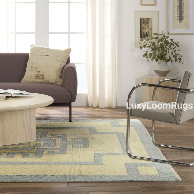 Pode incluir: Um tapete azul claro e amarelo com um design geom&eacute;trico. O tapete est&aacute; em uma sala de estar com um sof&aacute; e uma cadeira.