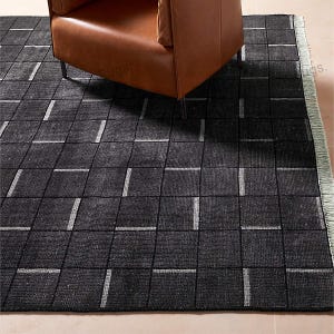 May include: A black and white checkered area rug with a fringe border. The rug has a subtle texture and is made of a soft material.