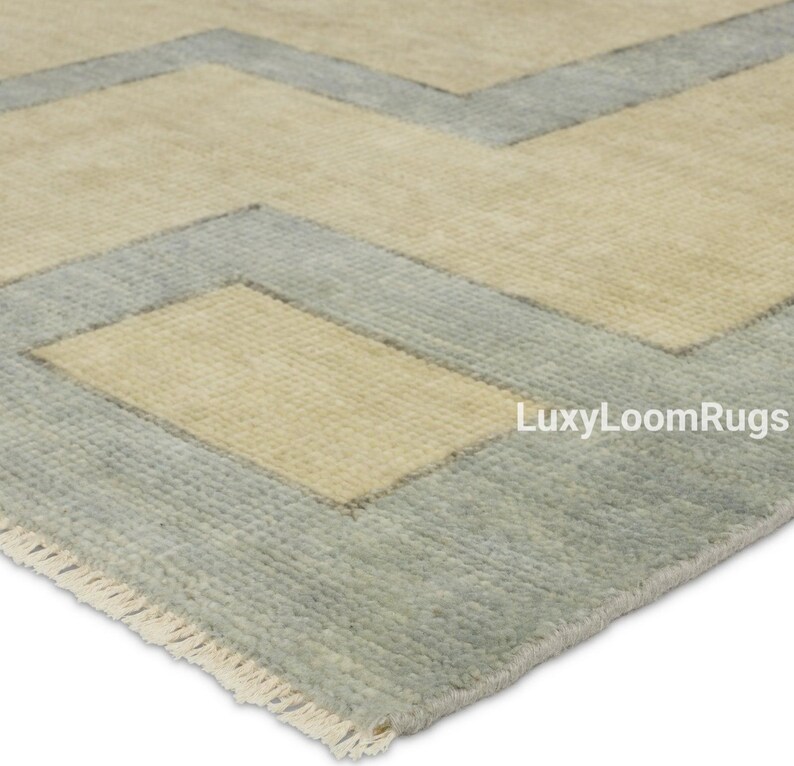 Pode incluir: Um tapete de &aacute;rea azul claro e bege com um padr&atilde;o geom&eacute;trico. O tapete tem uma borda de franjas e o texto "LuxyLoomRugs" &eacute; vis&iacute;vel no canto inferior direito.