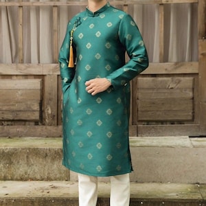 May include: A teal tunic with a mandarin collar and gold diamond pattern, paired with white pants and white sneakers. The tunic features long sleeves and a decorative tassel. The outfit is a traditional style.