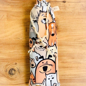 Op de afbeelding: Een witte trekkoordtas met een kleurrijke print van cartoonhonden. De tas is gemaakt van stof en heeft een trekkoord sluiting.