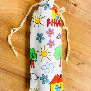 May include: A white drawstring bag with a colorful cartoon pattern of houses, suns, flowers, and clouds. The bag has a small brown tag with the text "Little Things" on it.