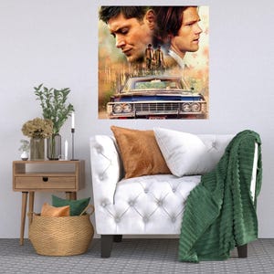 K&ouml;nnte beinhalten: Ein wei&szlig;es Sofa mit einer gr&uuml;nen Wolldecke und einem braunen Kissen. Ein Druck von zwei M&auml;nnern und einem Oldtimer h&auml;ngt an der Wand &uuml;ber dem Sofa.