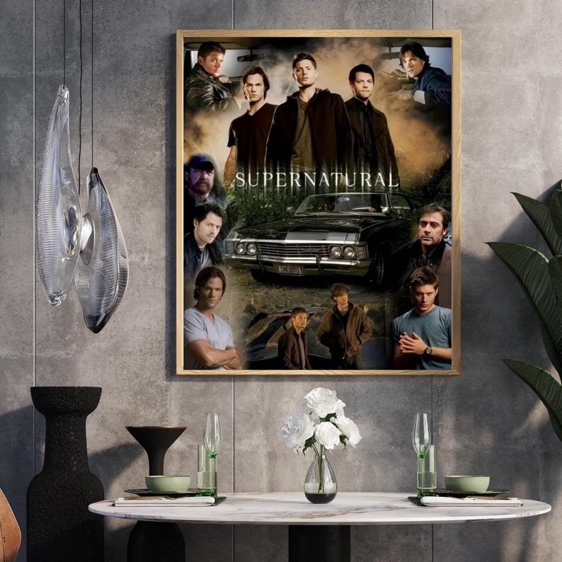 May include: A framed poster featuring multiple images of actors from the television show "Supernatural". The poster includes the show's title and a black car. The poster is displayed on a gray wall, with a table and decorative items in front.