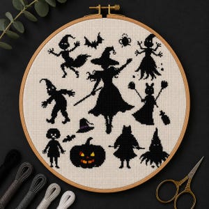 May include: A round wooden embroidery hoop containing a cross-stitch pattern on white fabric. The design features black silhouettes of various figures including a central witch, a pumpkin with orange eyes, bats, and other small spooky characters.