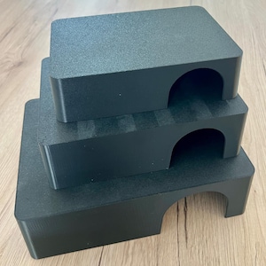 May include: Three-tiered black pet habitat steps with arched openings. The steps are stacked, decreasing in size from bottom to top. The textured surface of the steps provides a non-slip surface for pets. The steps are made of a solid, durable material.