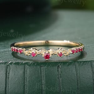 Op de afbeelding: Een delicate gouden band met een delicaat rankontwerp en kleine rode robijnstenen. De band is licht gebogen om aan de vinger te passen.