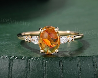 May include: A gold ring with an oval amber gemstone surrounded by small diamonds. The ring is set on a green surface.