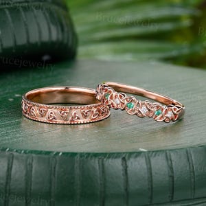 Könnte beinhalten: Zwei Ringe aus Roségold mit komplexen keltischen Knotenmustern. Ein Ring ist ein massives Band mit geprägten Knoten, während der andere ein zartes, durchbrochenes Band ist, das mit abwechselnd kleinen grünen und klaren weißen Steinen besetzt ist.