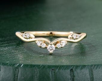 May include: A gold V-shaped ring featuring a central round-cut diamond flanked by two smaller diamonds on each side, with an additional pair of diamonds set along the curved band on both ends, creating a symmetrical leaf-like design.