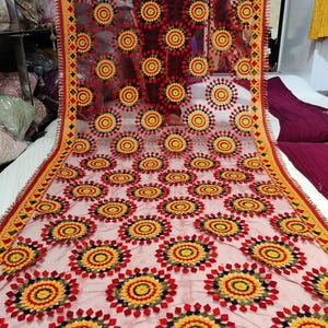 May include: A sheer, red shawl with a repeating pattern of embroidered floral medallions in yellow, red, and black. The edges are trimmed with a yellow and red geometric border and a red fringe.