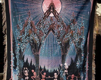 Könnte beinhalten: Eine schwarze Decke mit einem gotischen Kathedralen-Design, mit einem rosa Mond, tanzenden Skeletten und floralen Akzenten. Der Rand ist rosa mit Totenkopfmotiven und Fransen.