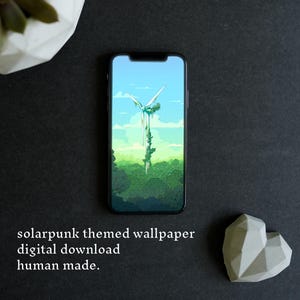 May include: A smartphone displaying a digital illustration of a wind turbine covered in green vines rising above a dense forest under a light blue sky. The screen shows the text: solarpunk themed wallpaper digital download human made.